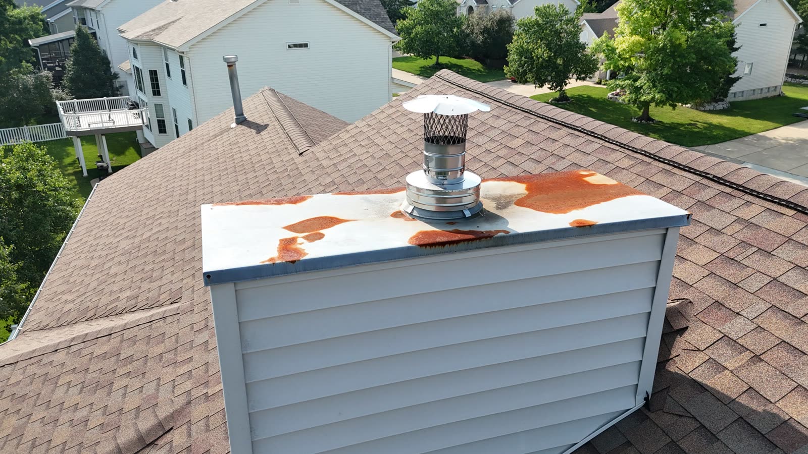 Wide view of a chimney chase with rust patches on the galvanized cover, the kind of corrosion visible from a roof inspection
