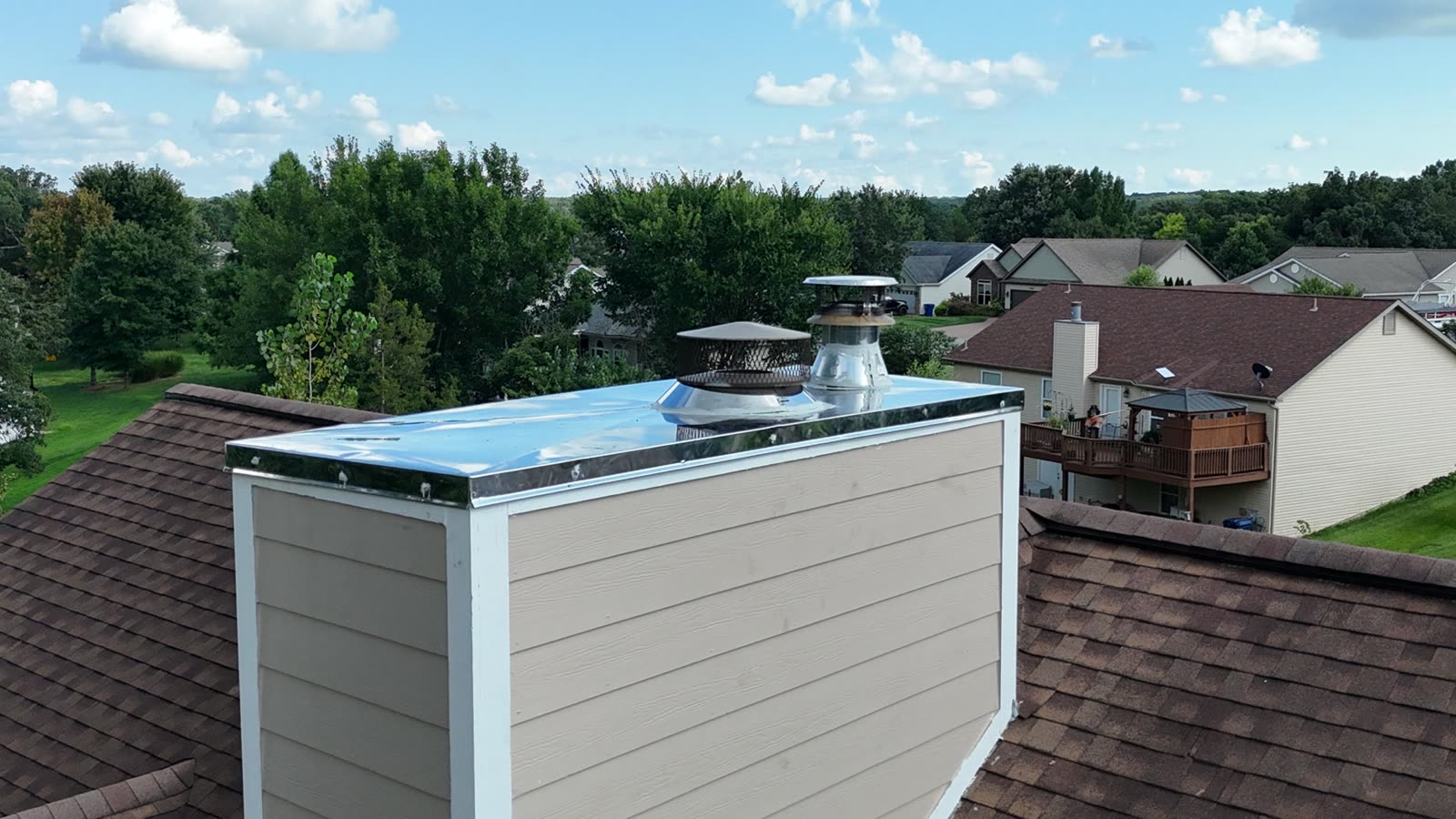 Completed two-flue stainless steel chase cover reflecting the sky, fitted around both vent penetrations