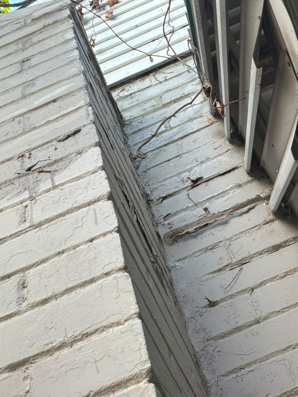Cracked and open mortar joints along the chimney ledge above the shoulder