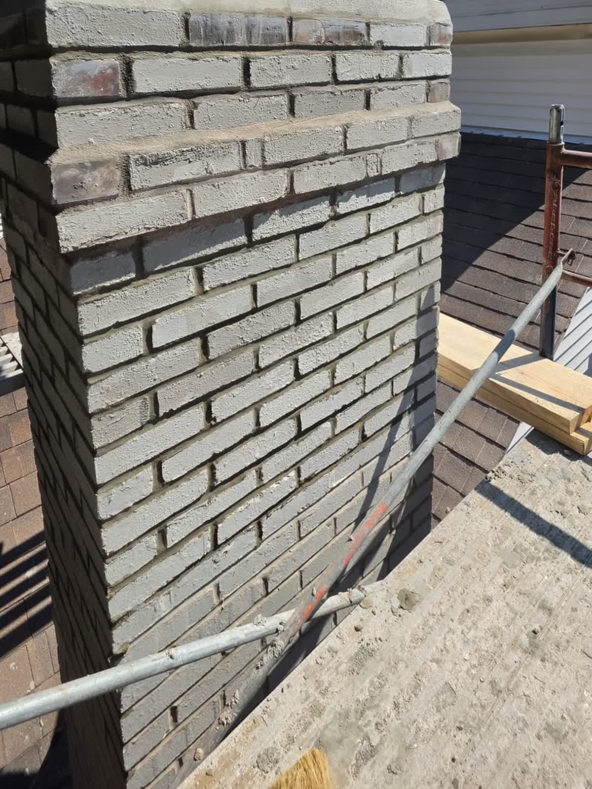 Staging planks and scaffold rails bridged across the roof slope alongside the rebuilt brickwork