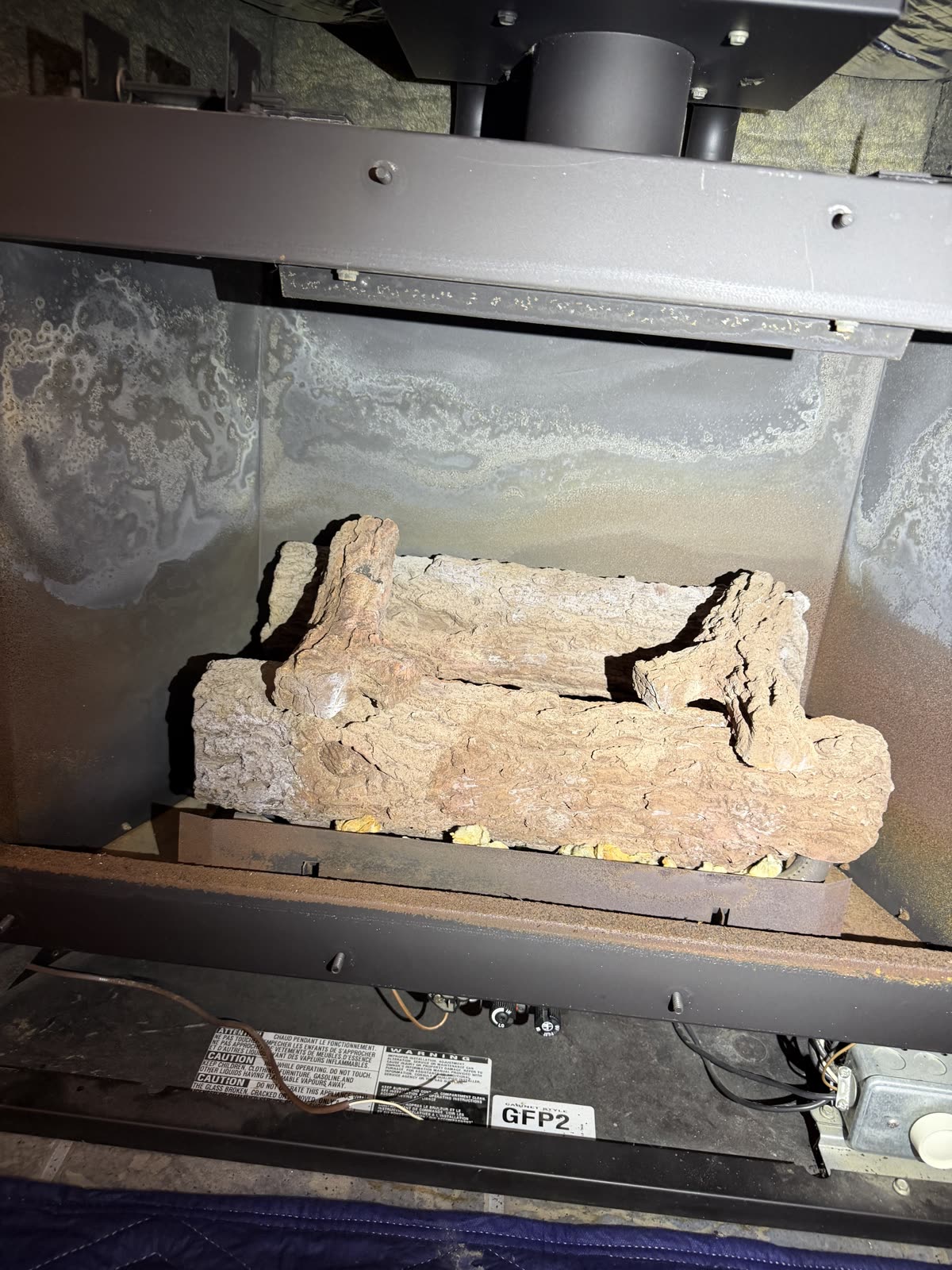 Gas fireplace before repair by AirPlease Missouri Chimney Services, with a worn log set and heavy mineral staining across the firebox panels